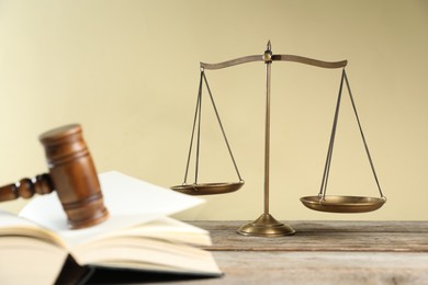 Photo of Golden scales of justice, gavel and book on wooden table against beige background, selective focus
