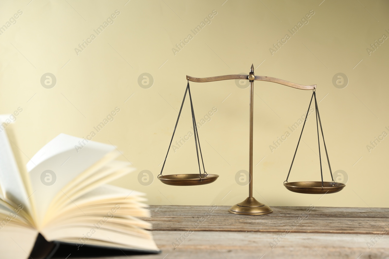 Photo of Golden scales of justice and book on wooden table against beige background, selective focus