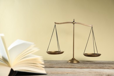 Photo of Golden scales of justice and book on wooden table against beige background, selective focus