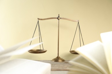 Photo of Golden scales of justice and books on wooden table against beige background, selective focus