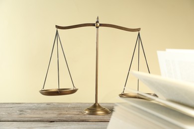 Photo of Golden scales of justice and book on wooden table against beige background, selective focus