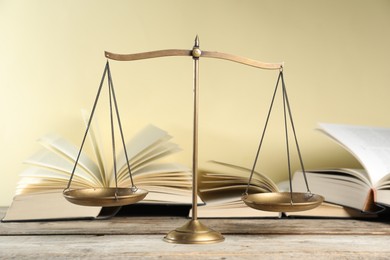 Photo of Golden scales of justice and books on wooden table against beige background