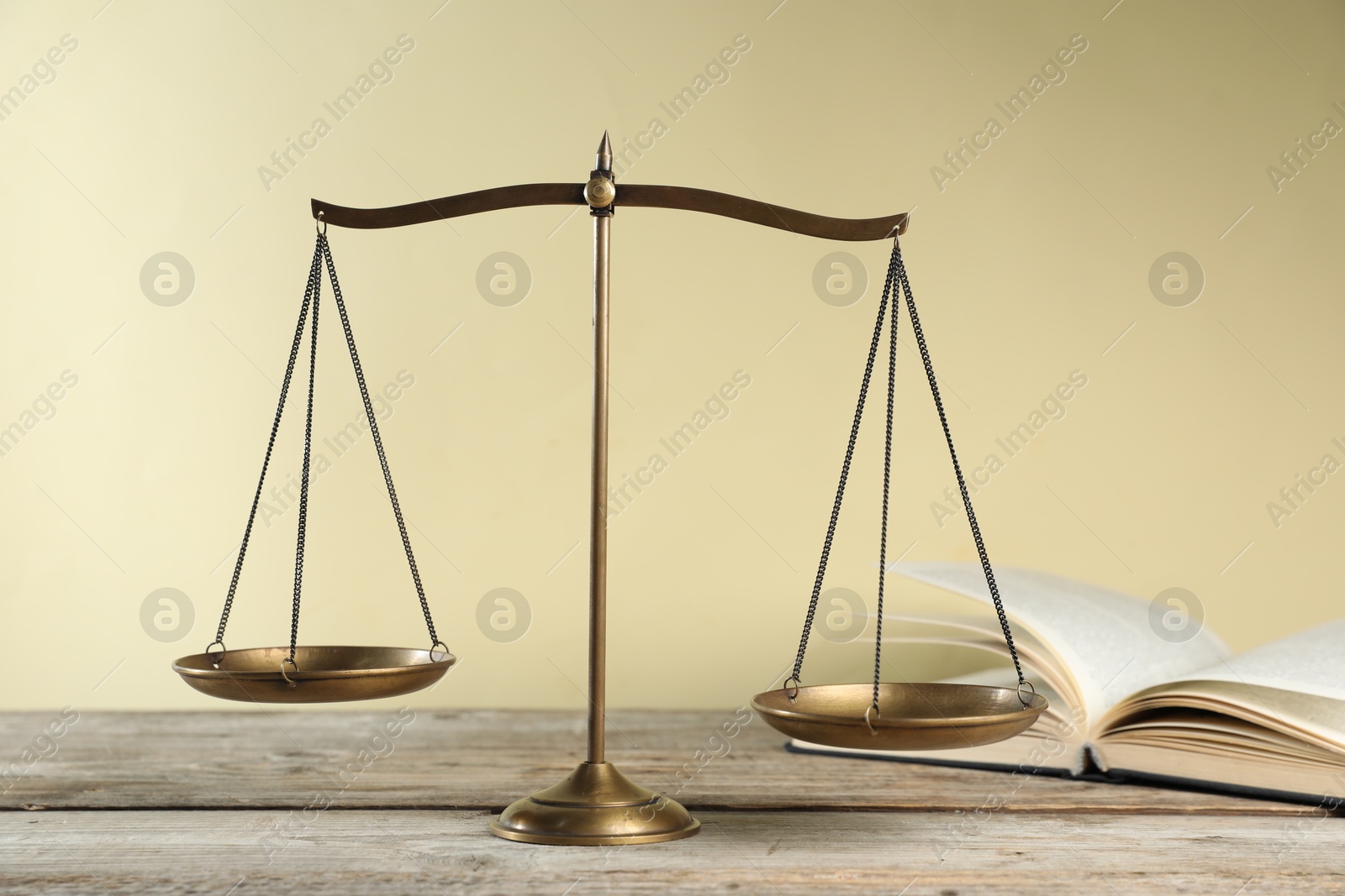 Photo of Golden scales of justice and book on wooden table against beige background