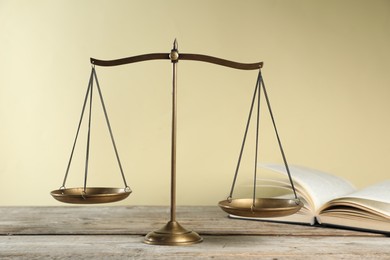 Photo of Golden scales of justice and book on wooden table against beige background