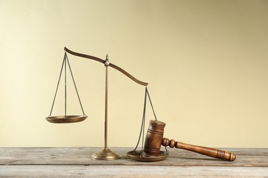 Photo of Golden scales of justice and gavel on wooden table against beige background