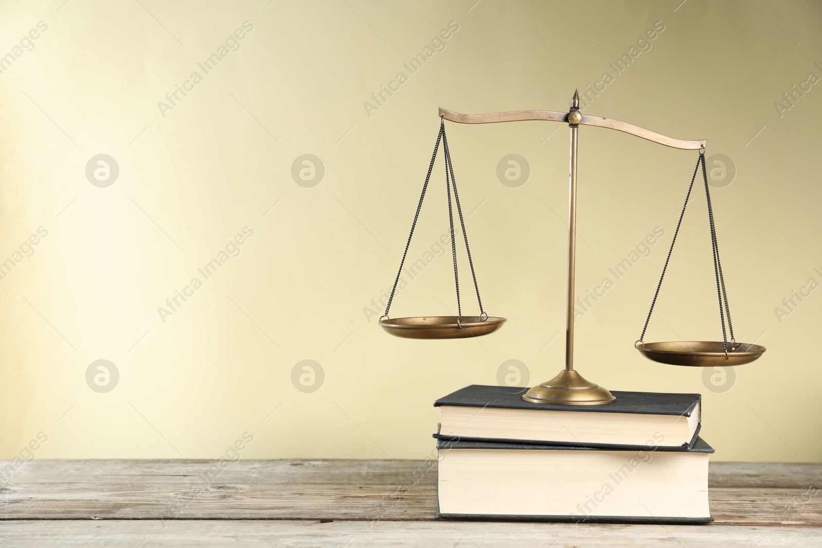 Photo of Golden scales of justice and books on wooden table against beige background, space for text