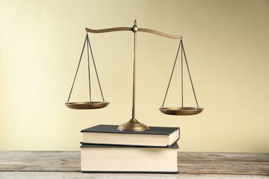 Photo of Golden scales of justice and books on wooden table against beige background