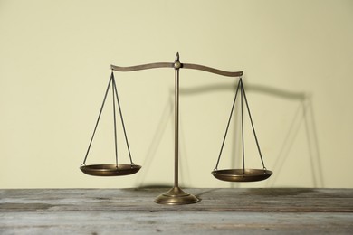 Photo of Golden scales of justice on wooden table against beige background