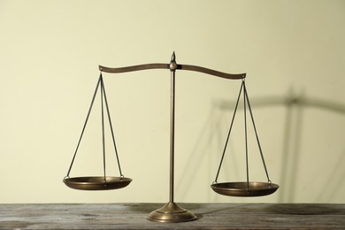 Photo of Golden scales of justice on wooden table against beige background