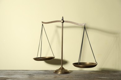 Photo of Golden scales of justice on wooden table against beige background