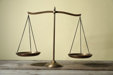 Photo of Golden scales of justice on wooden table against beige background