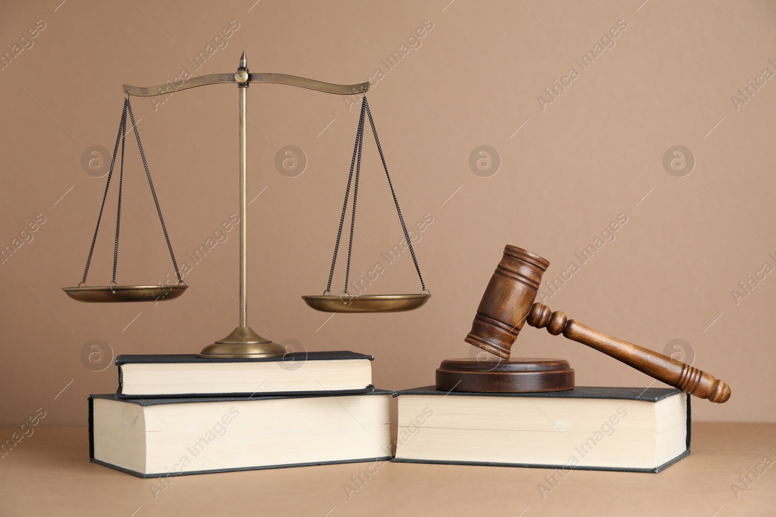 Photo of Golden scales of justice, books and gavel on light brown background