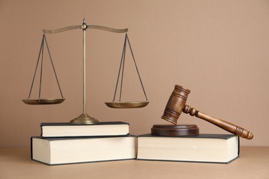 Photo of Golden scales of justice, books and gavel on light brown background
