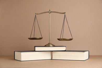 Photo of Golden scales of justice and books on light brown background
