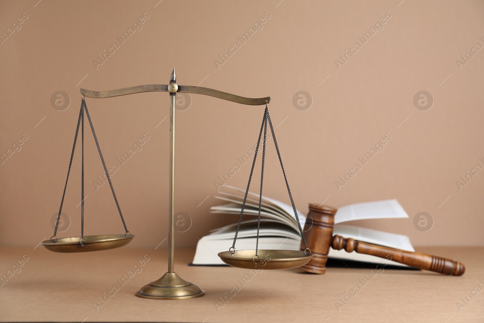 Photo of Golden scales of justice, book and gavel on light brown background