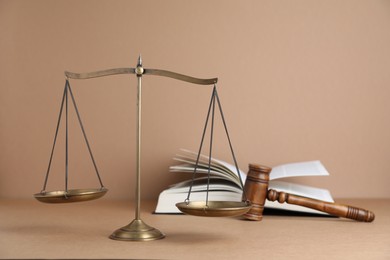 Photo of Golden scales of justice, book and gavel on light brown background