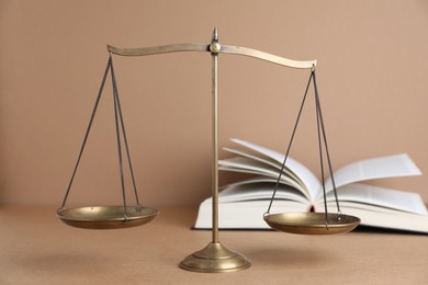 Photo of Golden scales of justice and book on light brown background