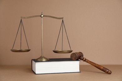 Photo of Golden scales of justice, book and gavel on light brown background