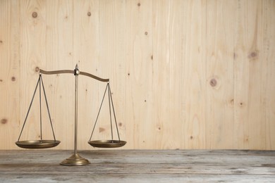 Photo of Golden scales of justice on wooden table, space for text
