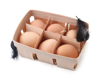 Photo of Raw chicken eggs and feathers in wooden egg tray isolated on white