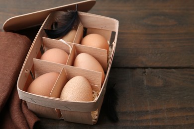 Photo of Raw chicken eggs in egg tray on wooden table, closeup. Space for text