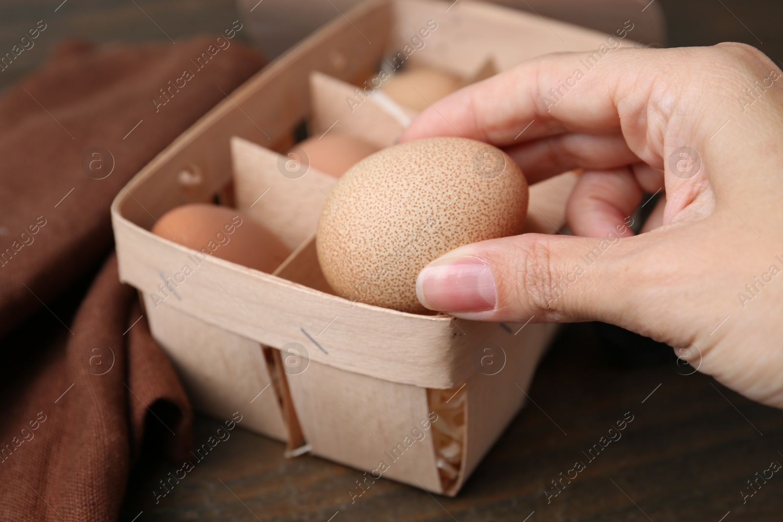 Photo of Woman taking raw chicken egg from tray at wooden table, closeup