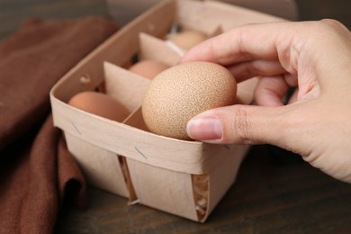 Photo of Woman taking raw chicken egg from tray at wooden table, closeup