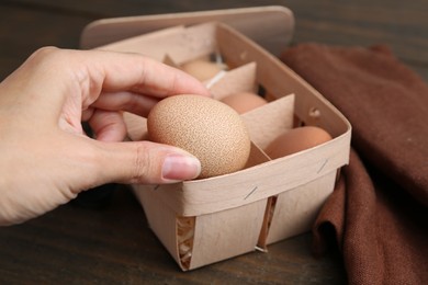 Photo of Woman taking raw chicken egg from tray at wooden table, closeup