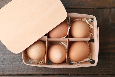 Photo of Raw chicken eggs in egg tray on wooden table, top view
