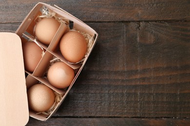 Photo of Raw chicken eggs in egg tray on wooden table, top view. Space for text