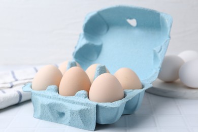 Photo of Raw chicken eggs in egg carton on white tiled table, closeup