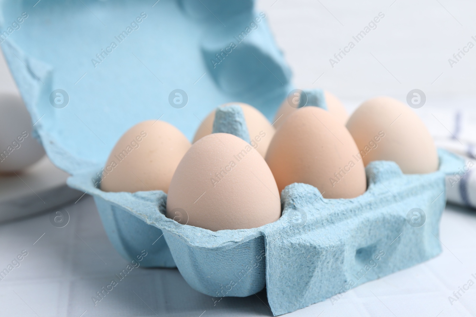Photo of Raw chicken eggs in egg carton on white tiled table, closeup