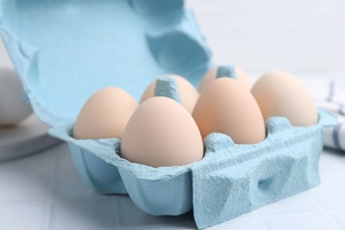 Photo of Raw chicken eggs in egg carton on white tiled table, closeup