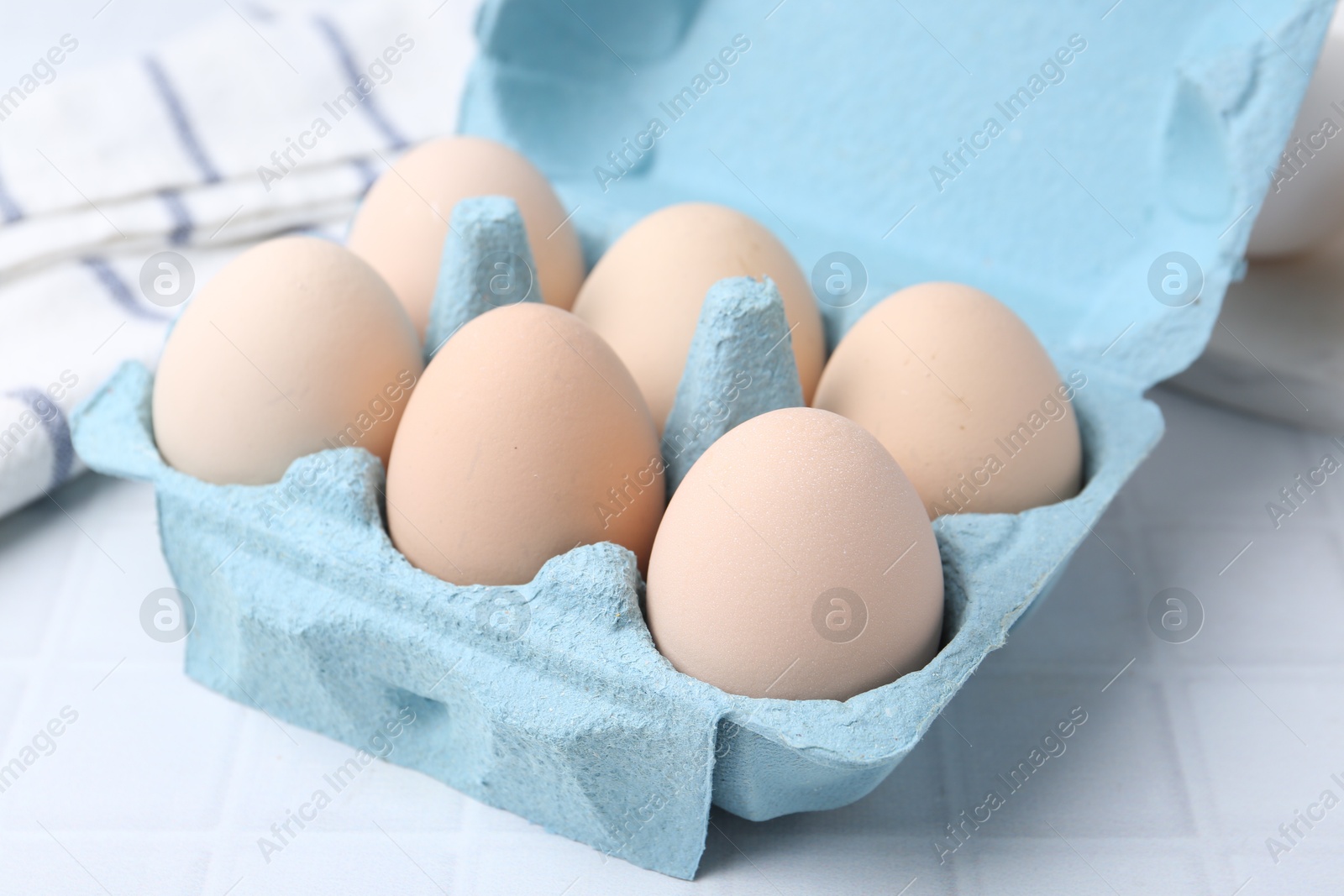 Photo of Raw chicken eggs in egg carton on white tiled table, closeup