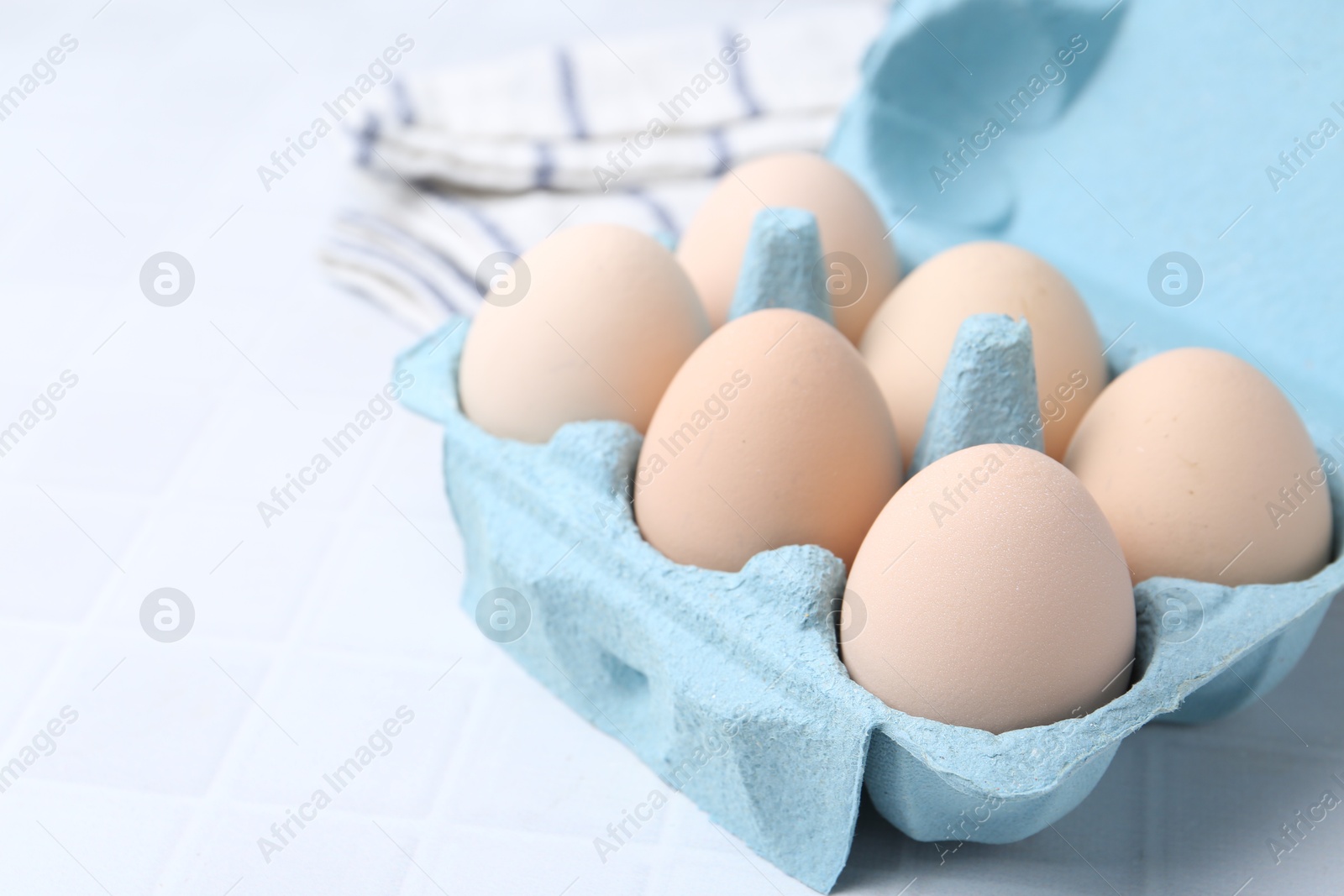 Photo of Raw chicken eggs in egg carton on white tiled table, closeup. Space for text