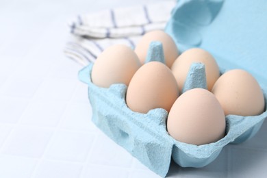 Photo of Raw chicken eggs in egg carton on white tiled table, closeup. Space for text