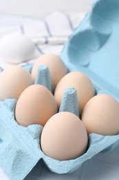 Photo of Raw chicken eggs in egg carton on white tiled table, closeup