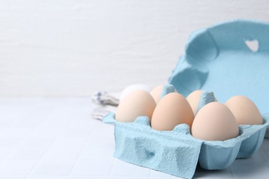 Photo of Raw chicken eggs in egg carton on white tiled table, closeup. Space for text