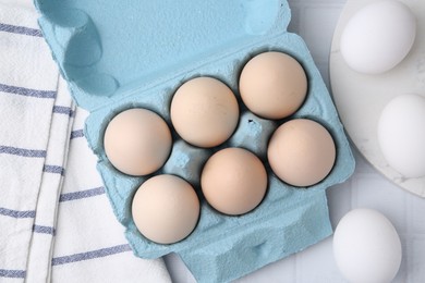 Photo of Raw chicken eggs in egg carton on white tiled table, flat lay