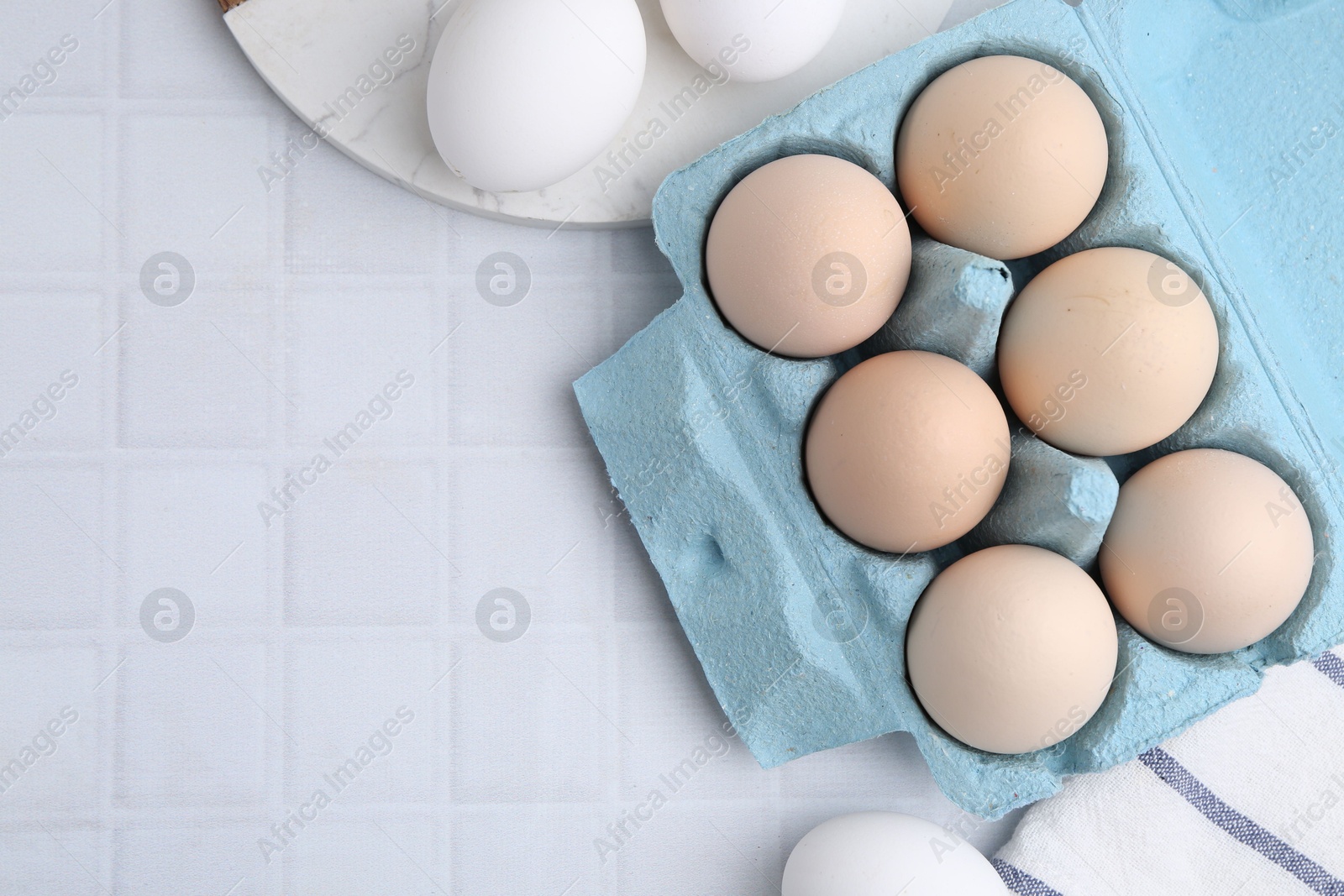 Photo of Raw chicken eggs in egg carton on white tiled table, flat lay. Space for text