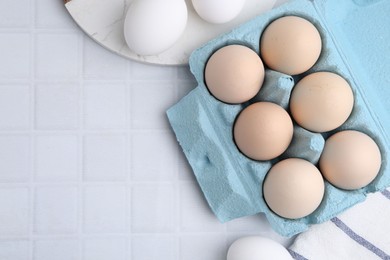 Photo of Raw chicken eggs in egg carton on white tiled table, flat lay. Space for text
