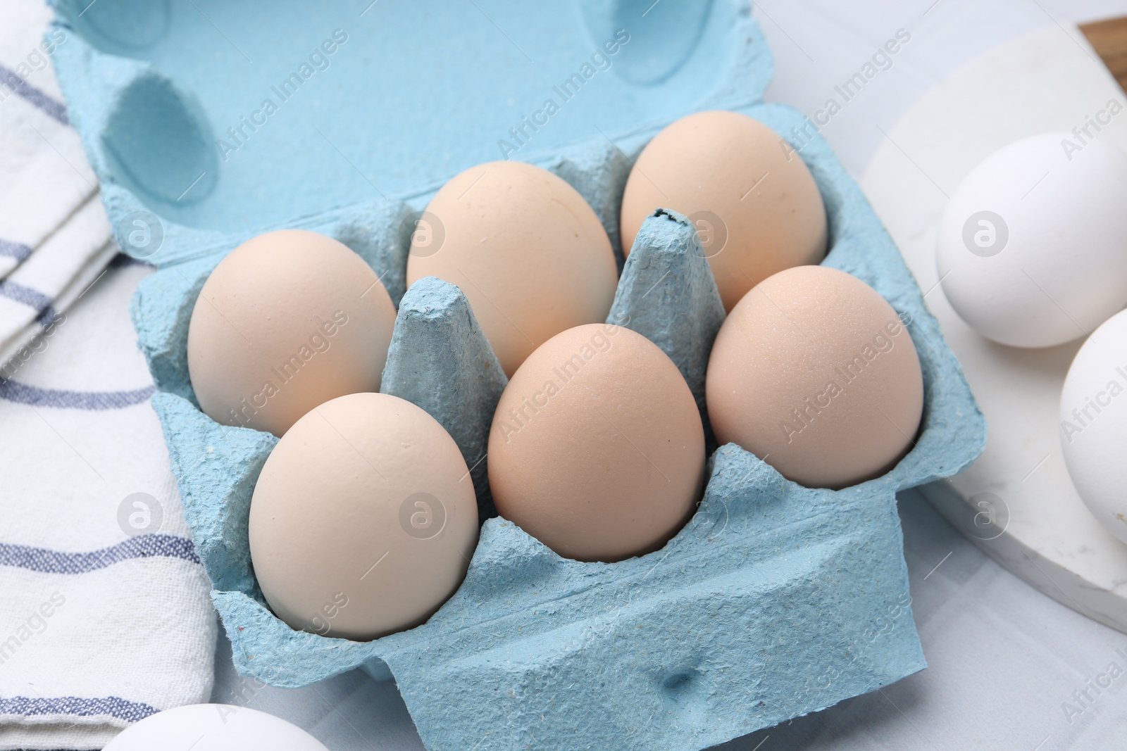 Photo of Raw chicken eggs in egg carton on white tiled table, closeup