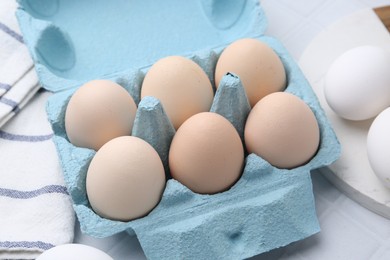 Photo of Raw chicken eggs in egg carton on white tiled table, closeup