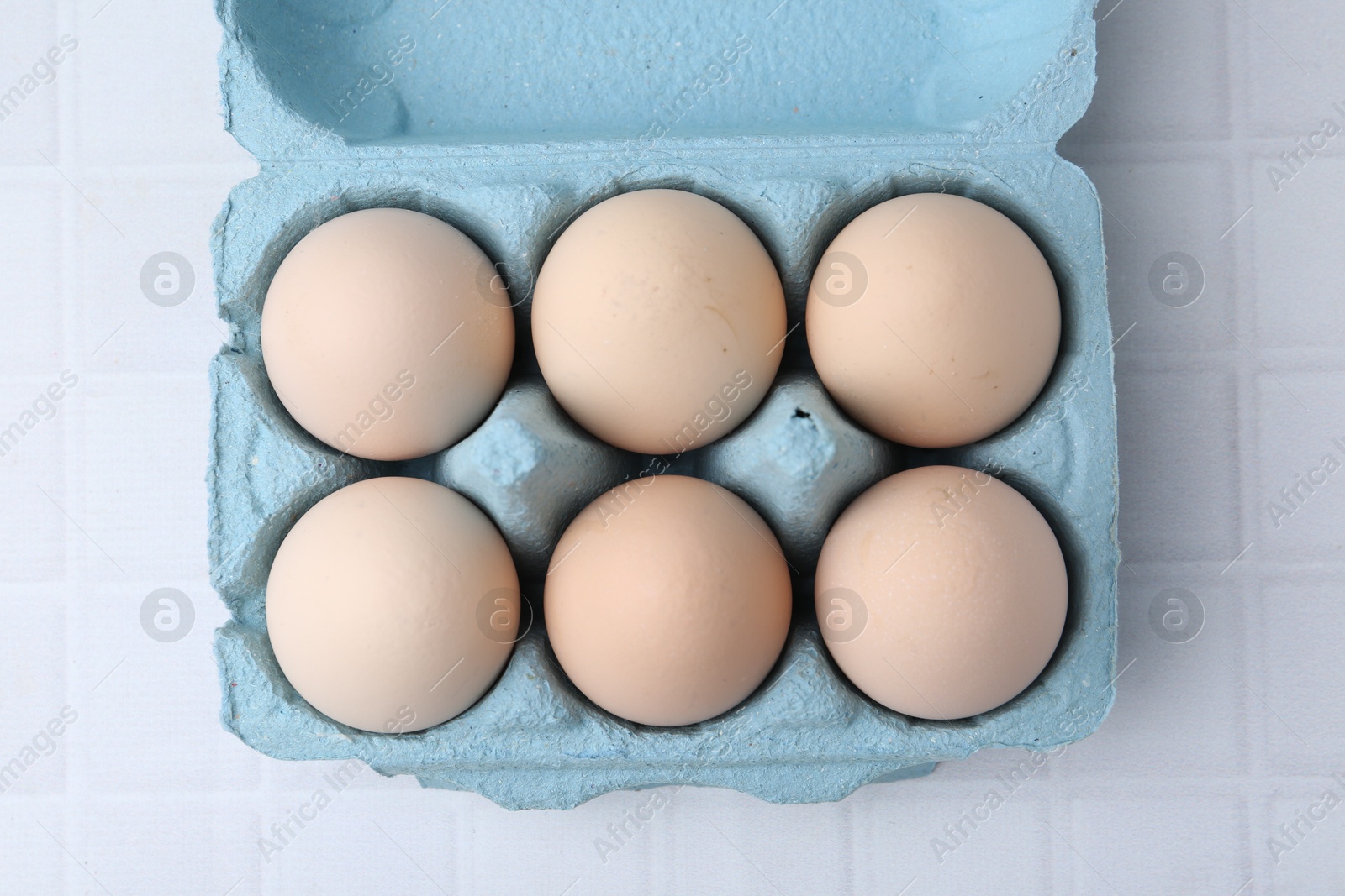 Photo of Raw chicken eggs in egg carton on white tiled table, top view