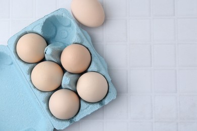 Photo of Raw chicken eggs in egg carton on white tiled table, flat lay. Space for text