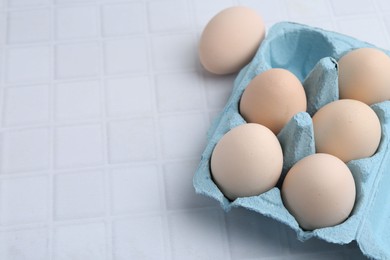 Photo of Raw chicken eggs in egg carton on white tiled table, closeup. Space for text