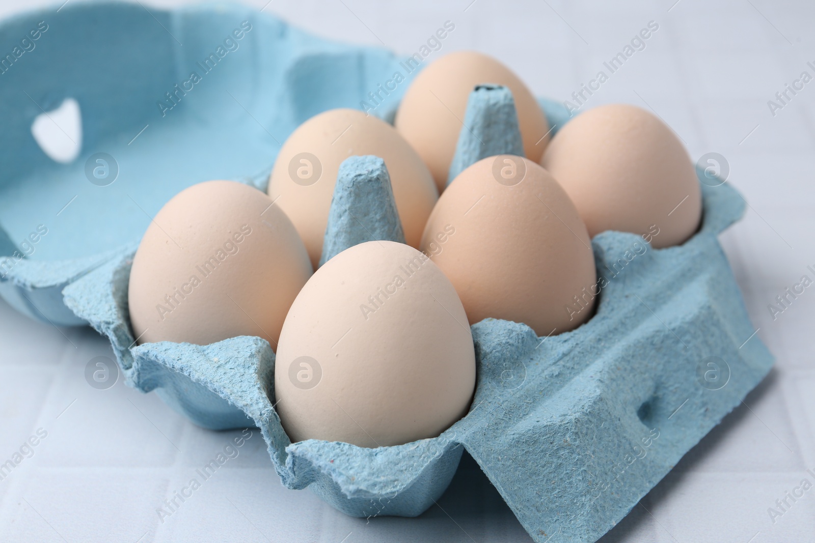 Photo of Raw chicken eggs in egg carton on white tiled table, closeup