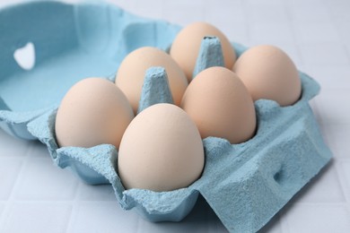 Photo of Raw chicken eggs in egg carton on white tiled table, closeup