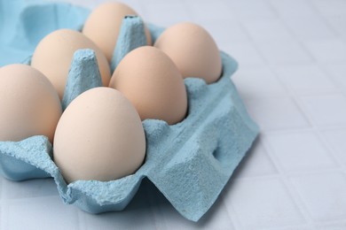 Photo of Raw chicken eggs in egg carton on white tiled table, closeup
