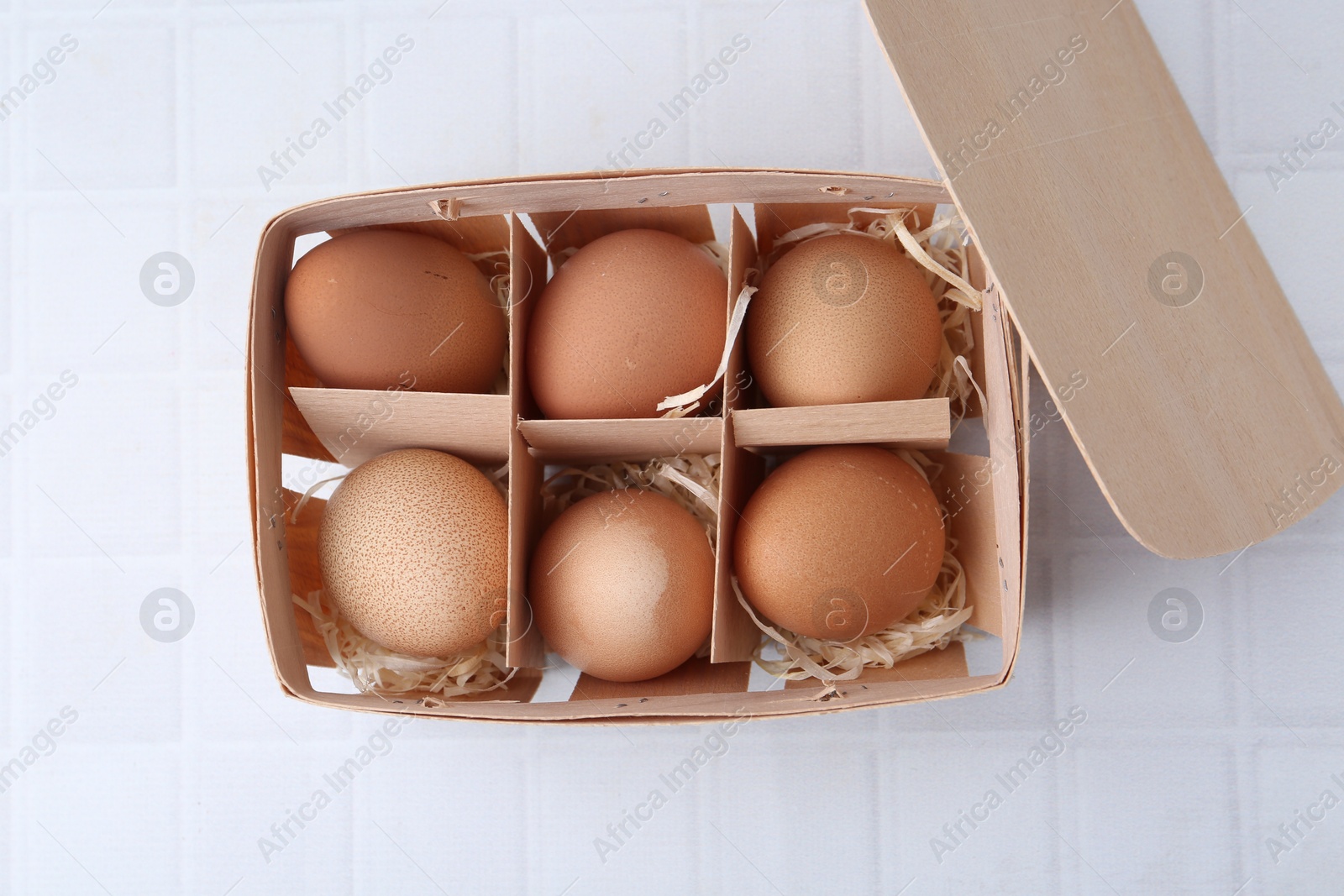Photo of Raw chicken eggs in wooden egg tray on white tiled table, top view